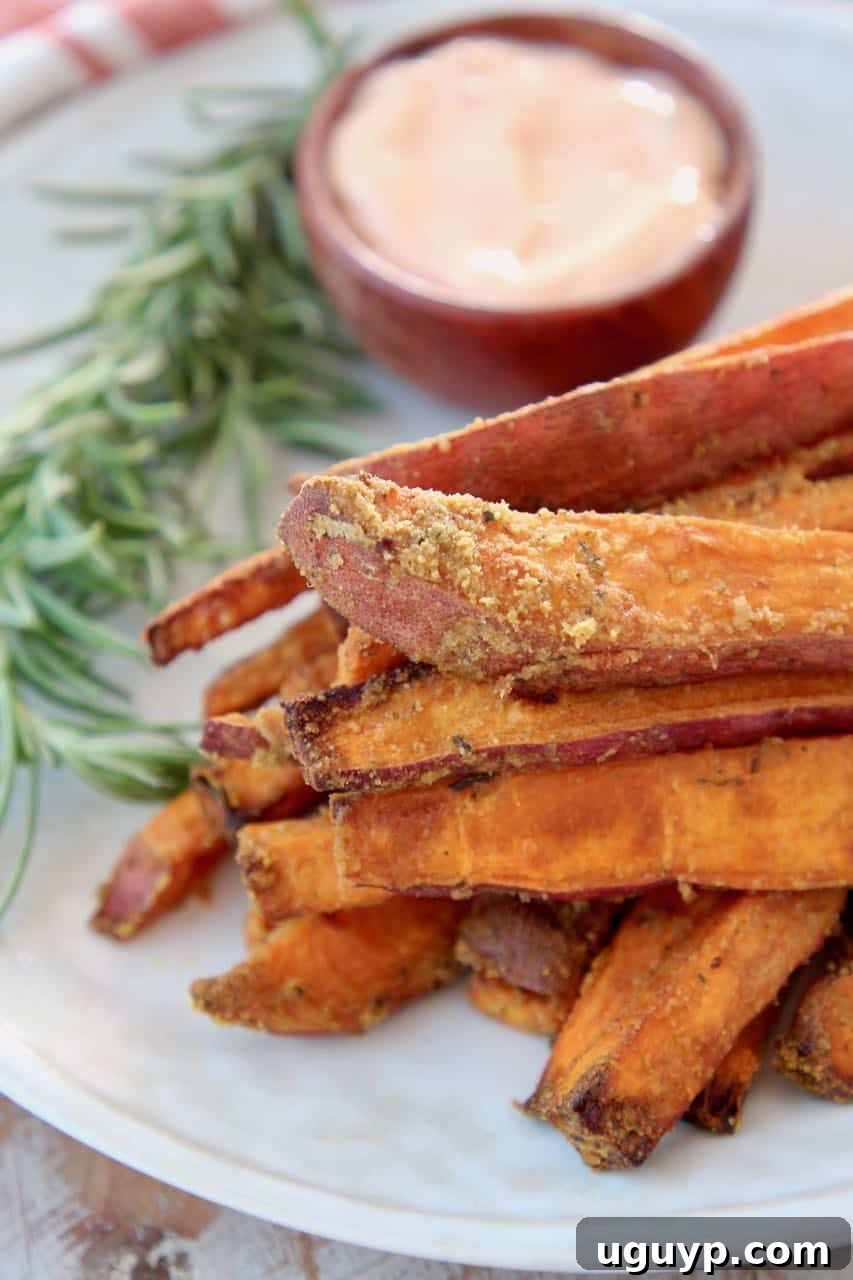 A stack of perfectly golden and crispy sweet potato fries on a white plate, garnished with a sprig of fresh rosemary.