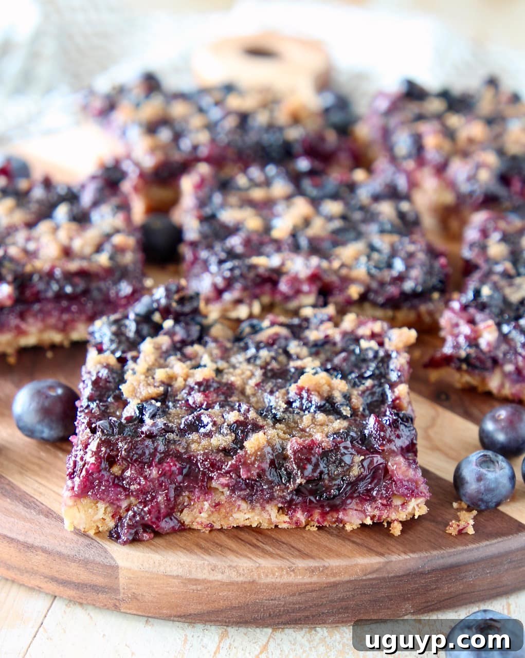 Golden brown blueberry oatmeal bars, freshly baked and cut into perfect squares, resting on a rustic wooden cutting board, surrounded by vibrant fresh blueberries.
