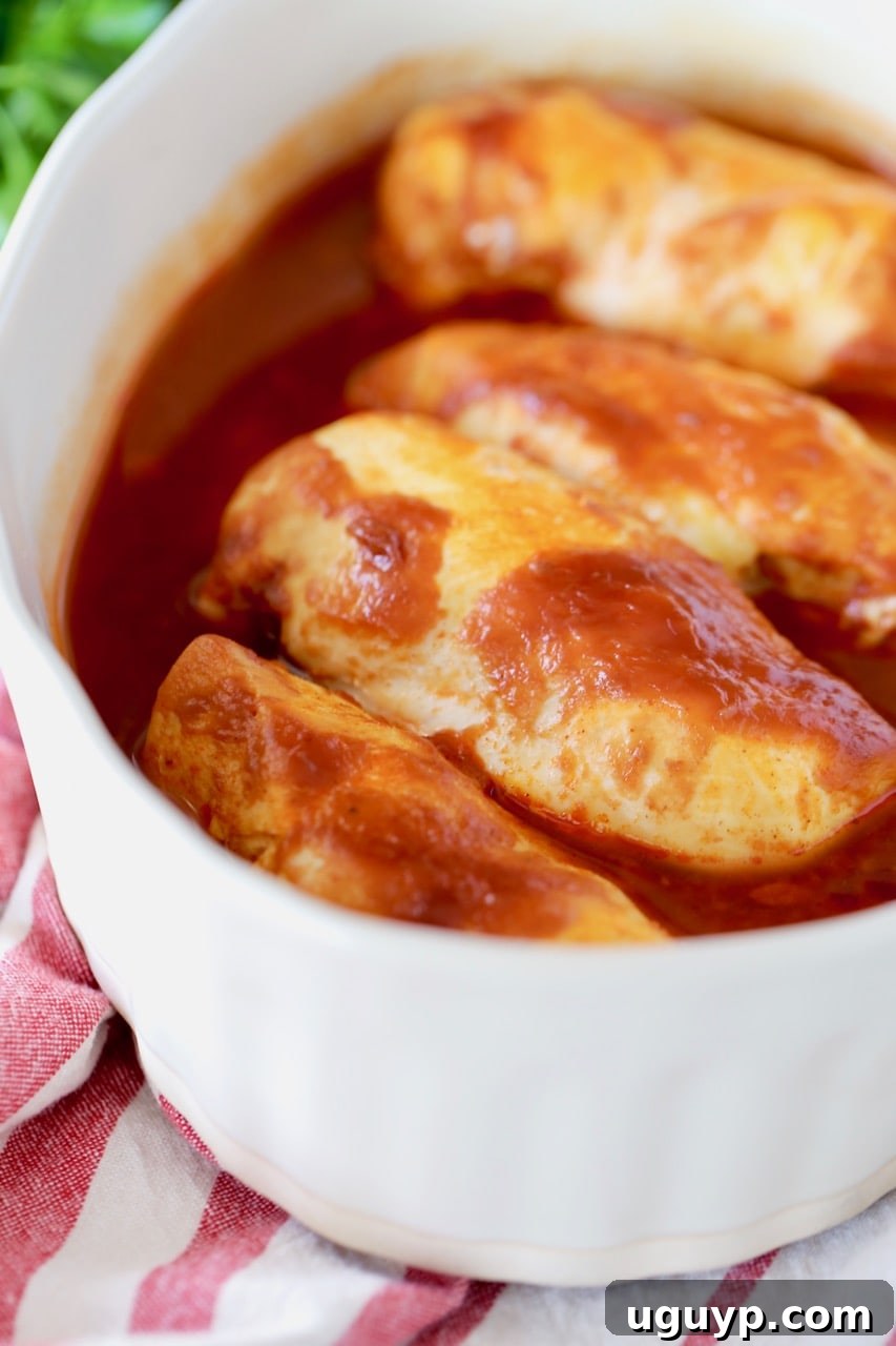 Baked chicken breasts in a beige casserole dish, richly covered in buffalo bbq sauce, resting on a vibrant red and white striped towel.