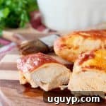 Baked Chicken covered in bbq and buffalo sauce, one piece sliced in half on wood cutting board with pastry brush in background