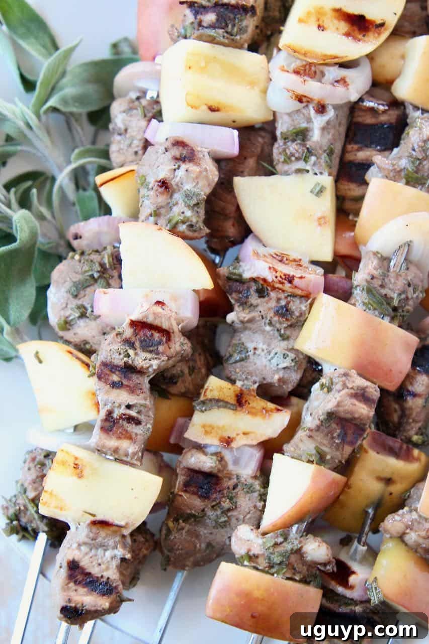 Close-up of raw pork tenderloin skewers with apples and shallots, ready for grilling, garnished with fresh herbs