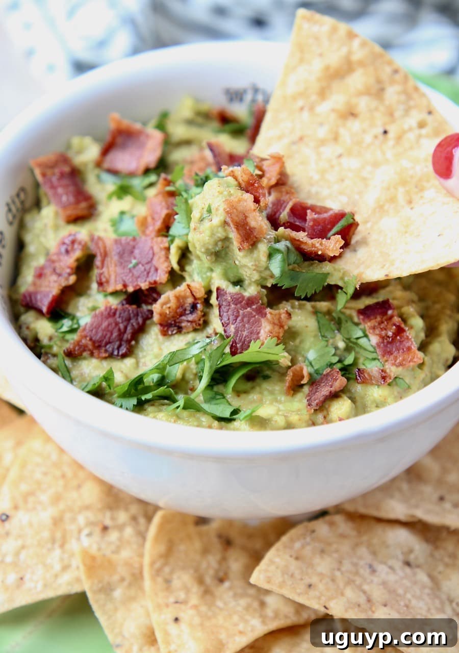 Tortilla chip expertly dipped into a bowl of rich Chipotle Bacon Guacamole, showcasing the creamy texture and bacon bits.