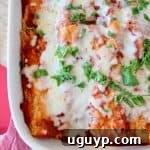 Close-up of a square baking dish filled with Italian enchiladas, ready for baking. The tortillas are rolled and topped with marinara sauce and shredded mozzarella cheese. A small bowl of fresh basil sits in the foreground.