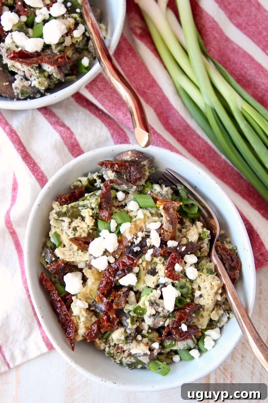 Flavorful Greek breakfast casserole with eggs, feta cheese, sun-dried tomatoes, and fresh green onions in serving bowls.