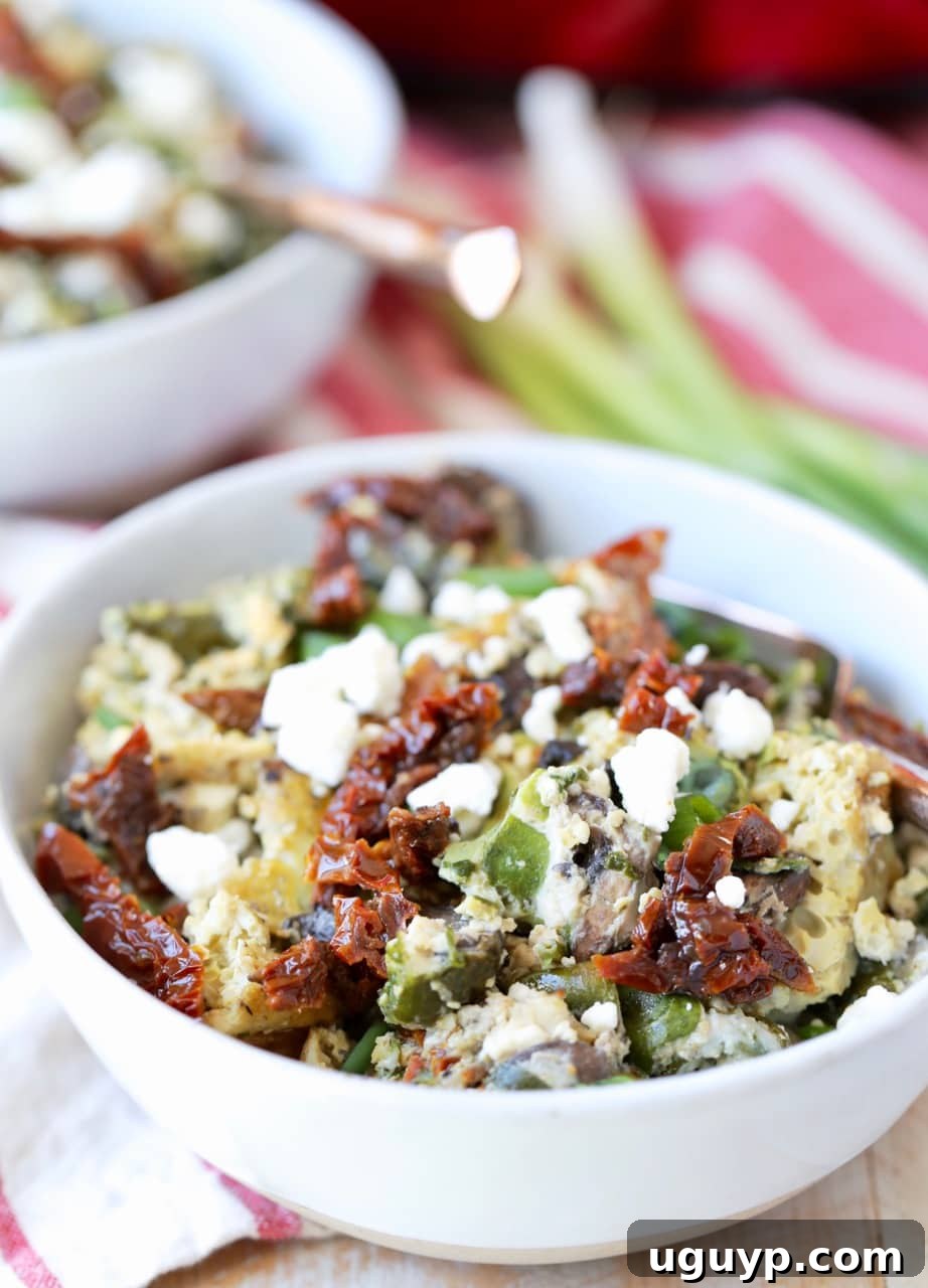 Close-up of a single serving of Greek egg casserole with feta and sun-dried tomatoes in a white bowl.