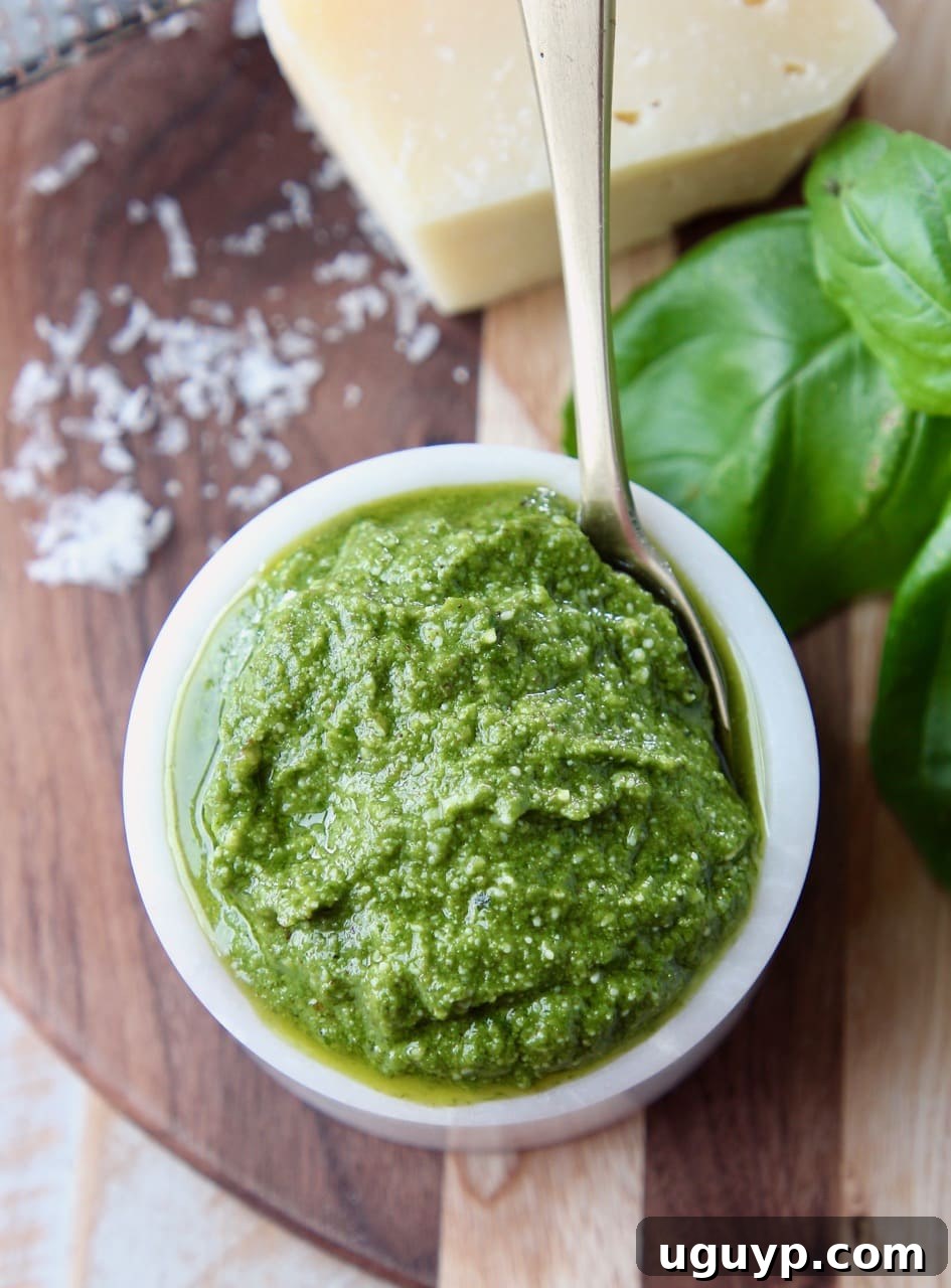 Overhead shot of basil pesto in a small white bowl with a small gold spoon in the bowl