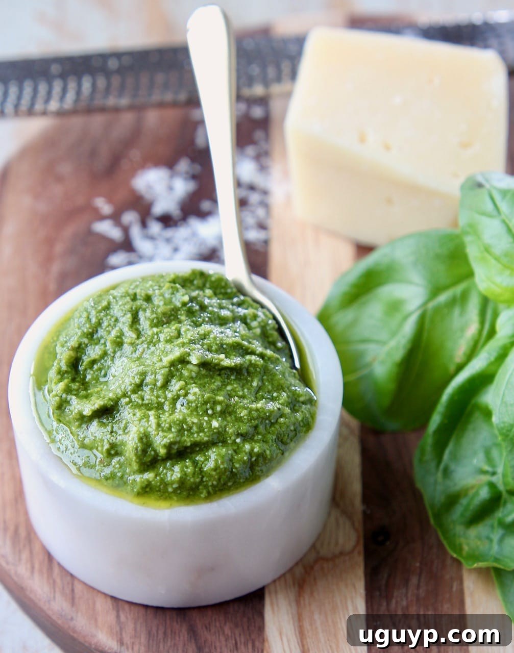 Basil pesto in small white bowl sitting next to fresh basil leaves and a block of parmesan cheese