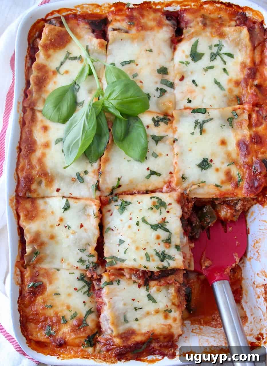 overhead image of lasagna in casserole dish cut into squares with red spatula