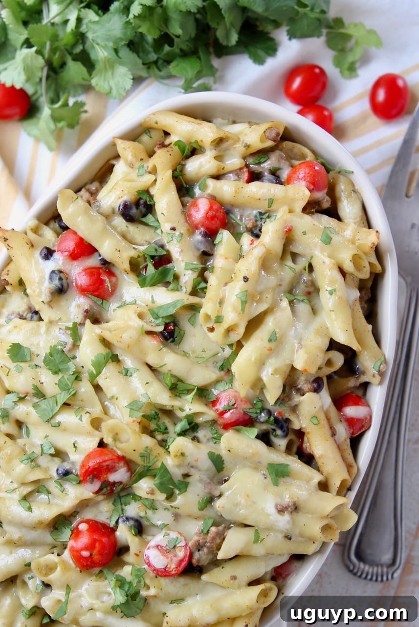 A close-up shot of the baked taco pasta in a casserole dish, showing the vibrant black beans, cherry tomatoes, and fresh cilantro garnish.