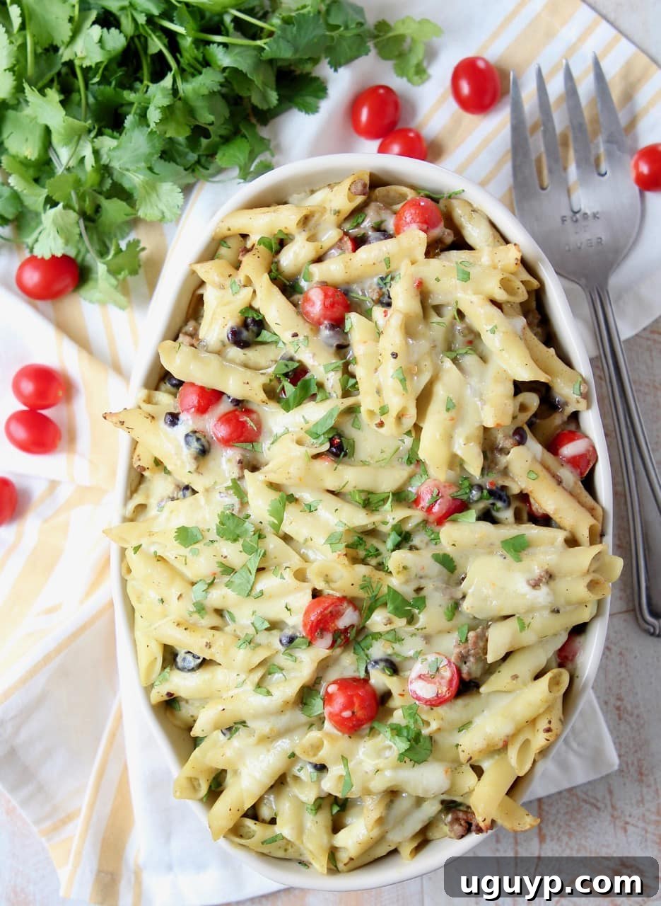 A close-up of a serving of Taco Pasta Bake in an oval casserole dish, with a fork digging in, and cherry tomatoes on the side.