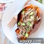A plate featuring a roasted sweet potato generously filled with pulled pork, accompanied by a fork, ready to be enjoyed.