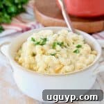 Butternut squash mac and cheese in white bowl with gold spoon on orange striped towel with fresh parsley
