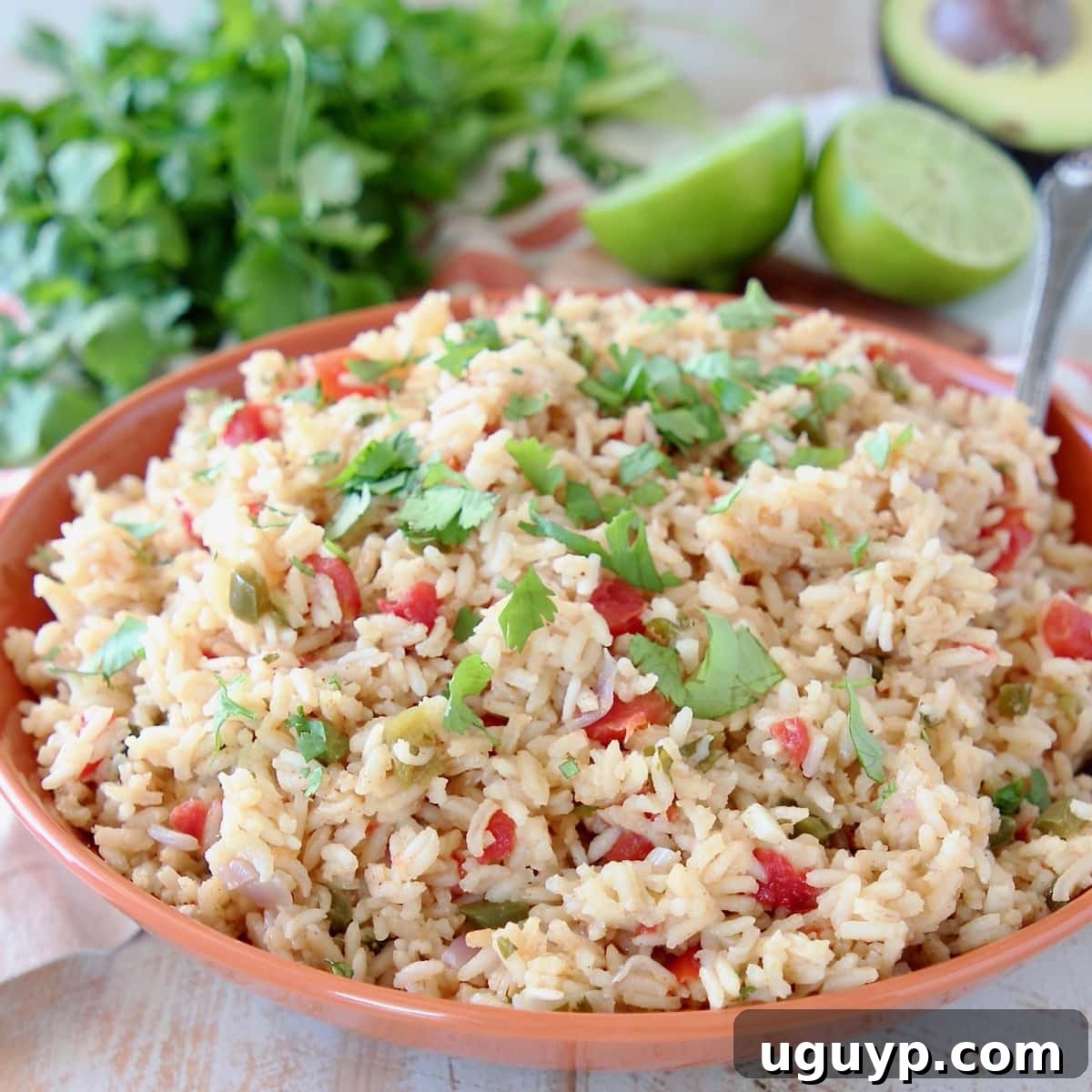 Vibrantly colored Mexican rice in an orange bowl, garnished with fresh cilantro and lime wedges, ready to serve.