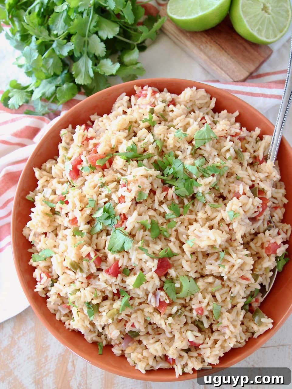 A serving of fluffy Mexican rice topped generously with vibrant fresh cilantro, in an orange ceramic bowl with a wooden serving spoon.