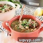 Greek turkey soup with chickpeas and spinach in orange bowl with sliced lemon