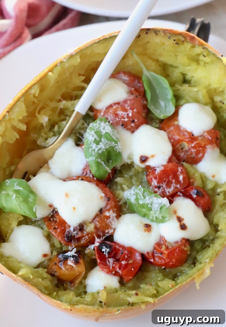 Close-up of a roasted spaghetti squash half beautifully stuffed with pesto-coated squash strands, sweet roasted cherry tomatoes, fresh basil, and perfectly melted mozzarella cheese.
