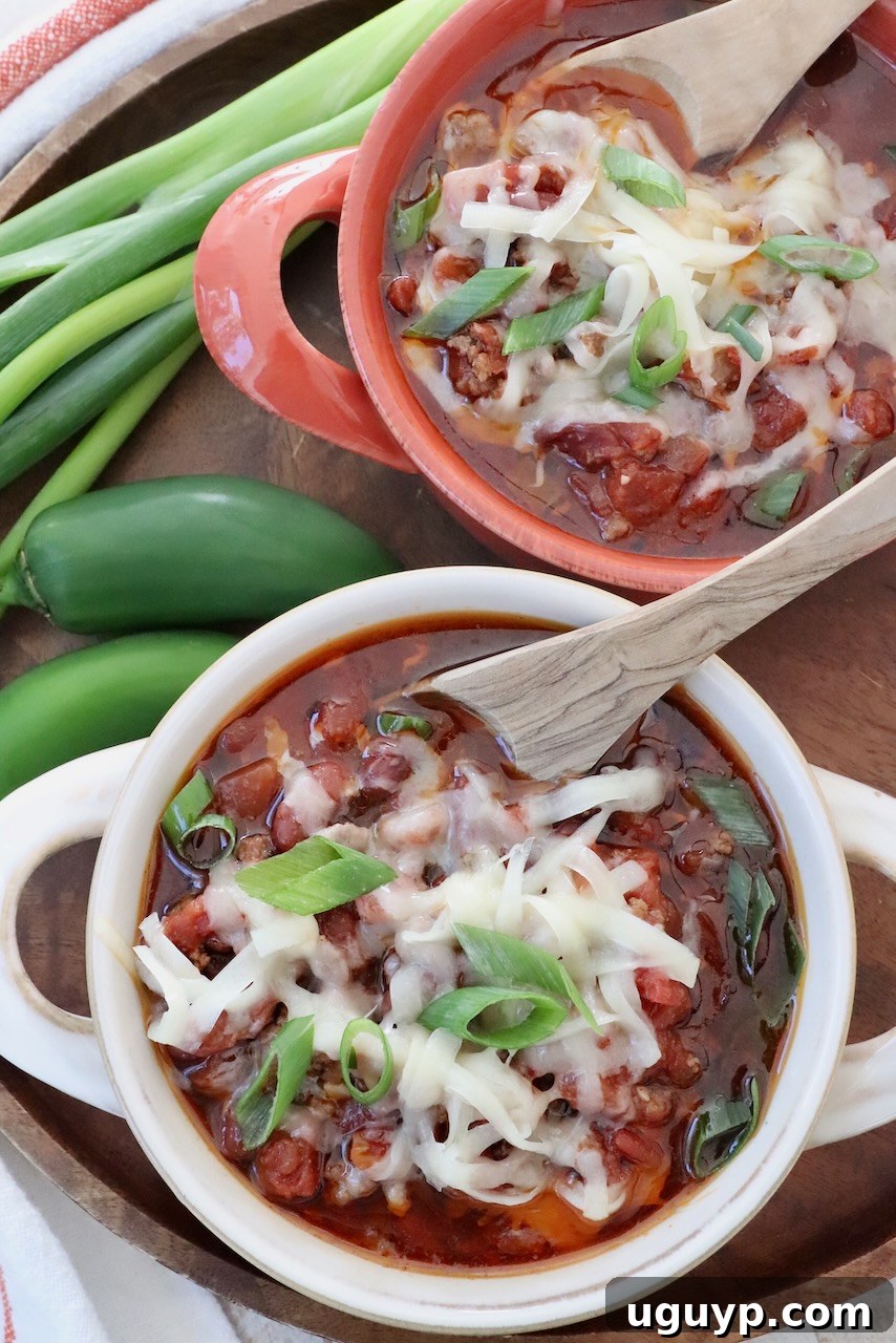 chili in bowls with spoons topped with shredded cheese and diced green onions
