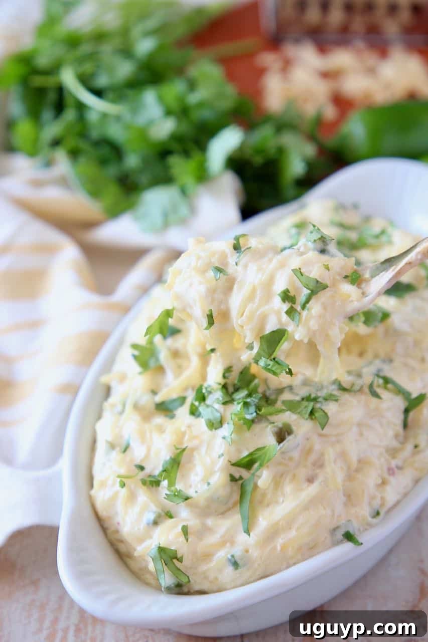 Fork coming out of bowl of roasted spaghetti squash with cheese sauce, topped with fresh cilantro.