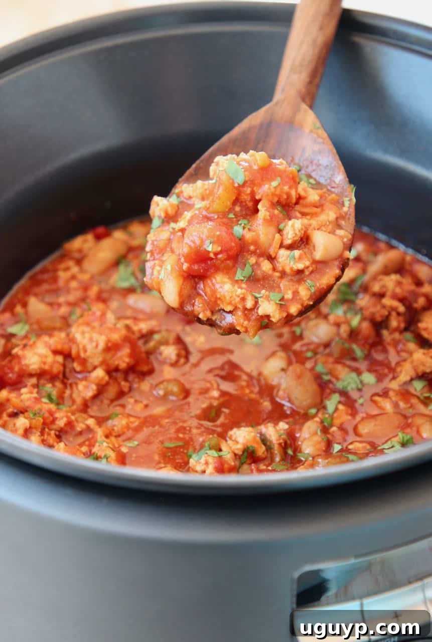 Buffalo chicken chili in a spoon coming out of a slow cooker