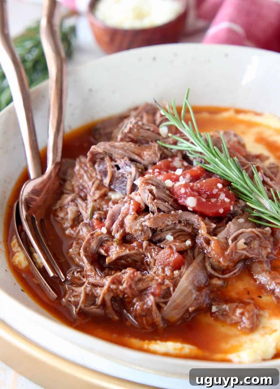 Shredded beef ragu in bowl served over polenta with fresh rosemary