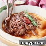 Shredded beef ragu tomato sauce in bowl with creamy polenta and rosemary sprig