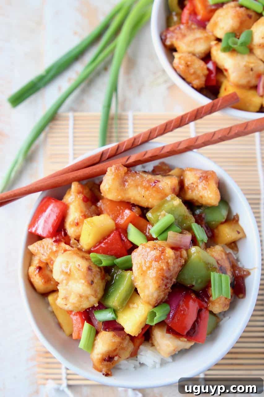 Sweet and sour chicken with pineapple and bell peppers on top of rice in bowl with chopsticks on the side