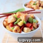 Sweet and sour chicken with bell peppers and pineapple chunks in bowl with chopsticks