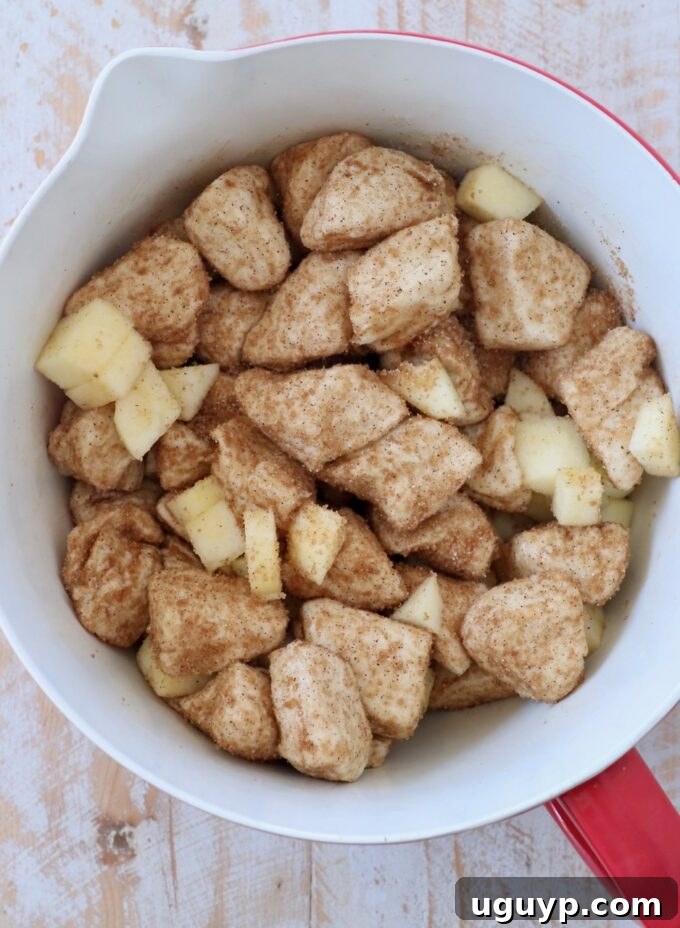 Diced apples tossed with cinnamon sugar-coated biscuit dough pieces in a mixing bowl.