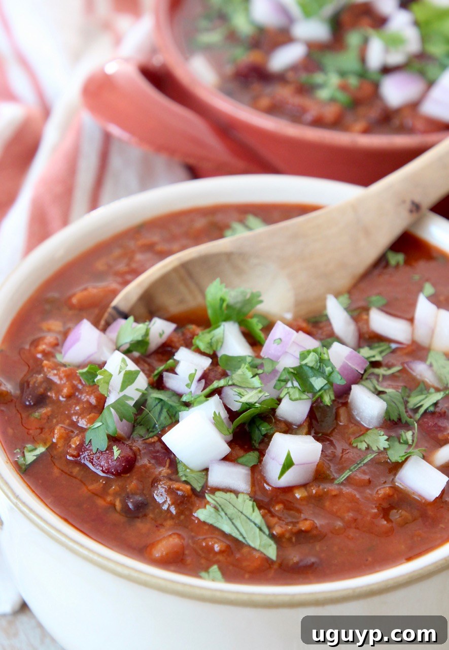 A hearty bowl of three-bean vegan chili with a spoon, highlighting its thick and satisfying texture.