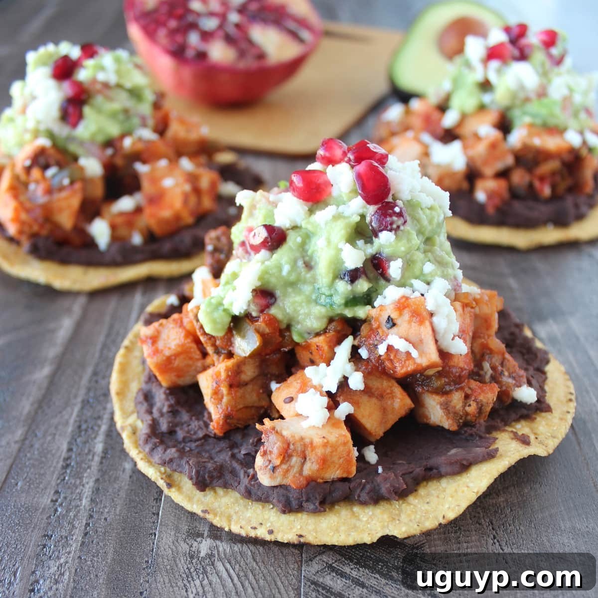 Close-up of a fully assembled turkey tostada, showcasing layers of beans, seasoned turkey, and a generous dollop of pomegranate guacamole.