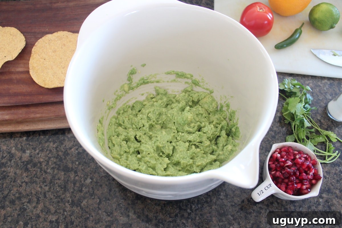 Freshly mashed avocado in a large mixing bowl, ready for the next ingredients.