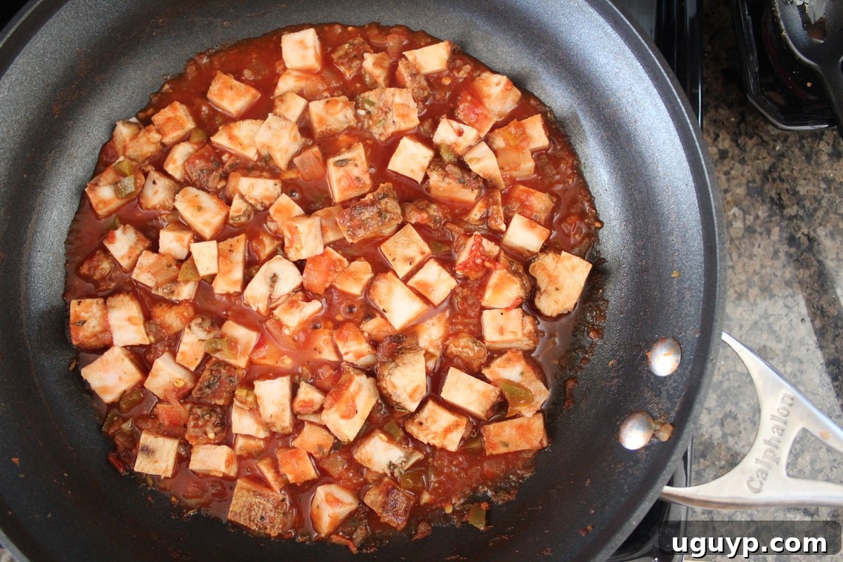 Diced cooked turkey simmering in a skillet with red salsa, heating up on a stovetop.