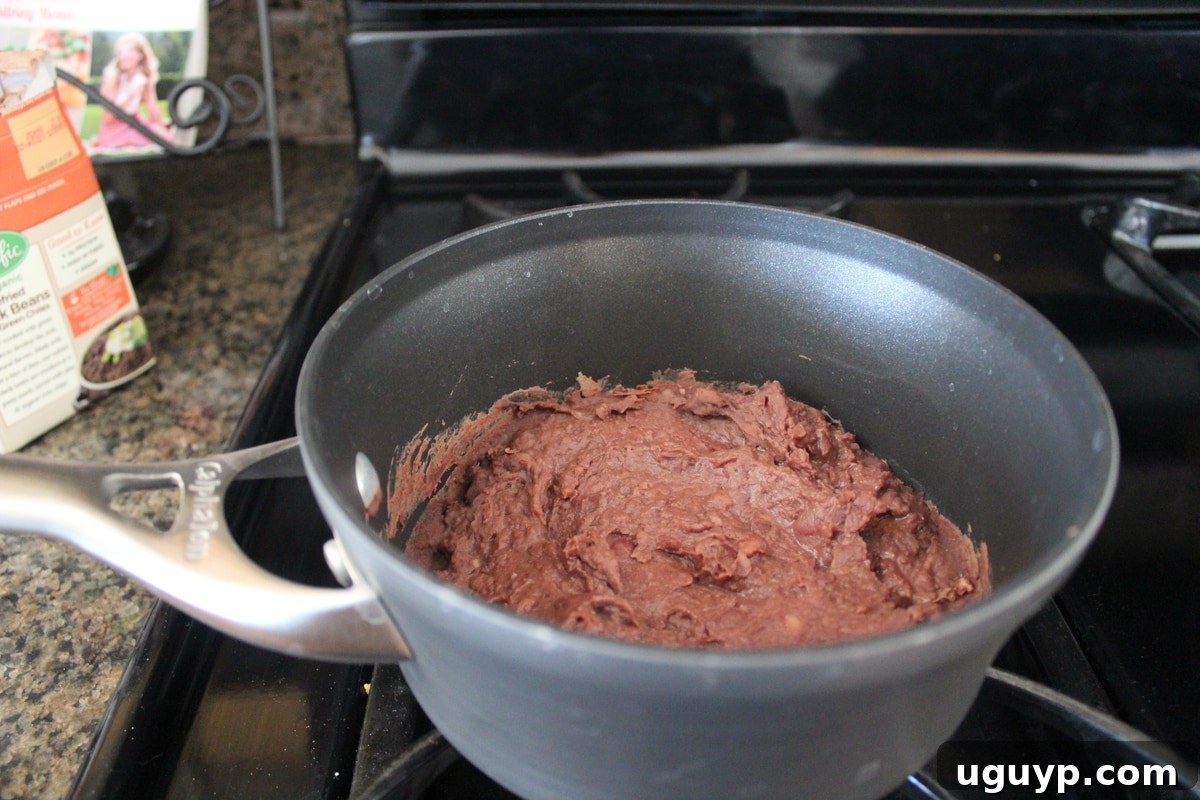 Refried black beans bubbling gently in a small saucepan on a burner, being heated to perfection.