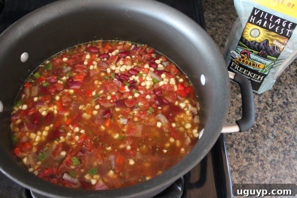 Pouring vegetable broth over the freekeh and vegetable mixture in the pot.
