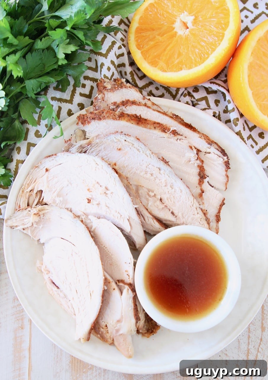 Slices of turkey breast on a white plate, with a side ramekin of orange bourbon glaze with sliced orange in background and fresh parsley bunch