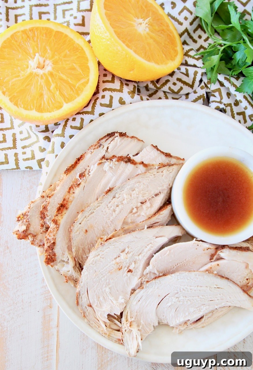 Slices of spice rubbed turkey breast on plate, next to small white bowl or orange bourbon sauce, with an orange cut in half next to the plate with fresh parsley