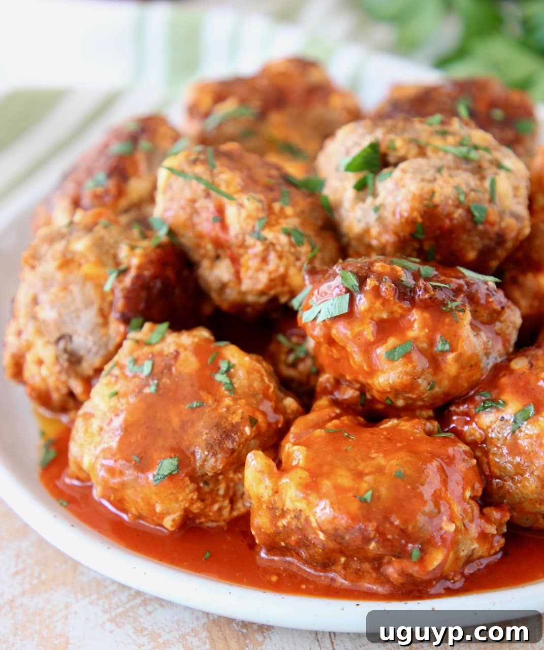 Cheesy Sausage Balls with Buffalo Sauce and Cilantro Garnish on Plate with Green Striped Towel