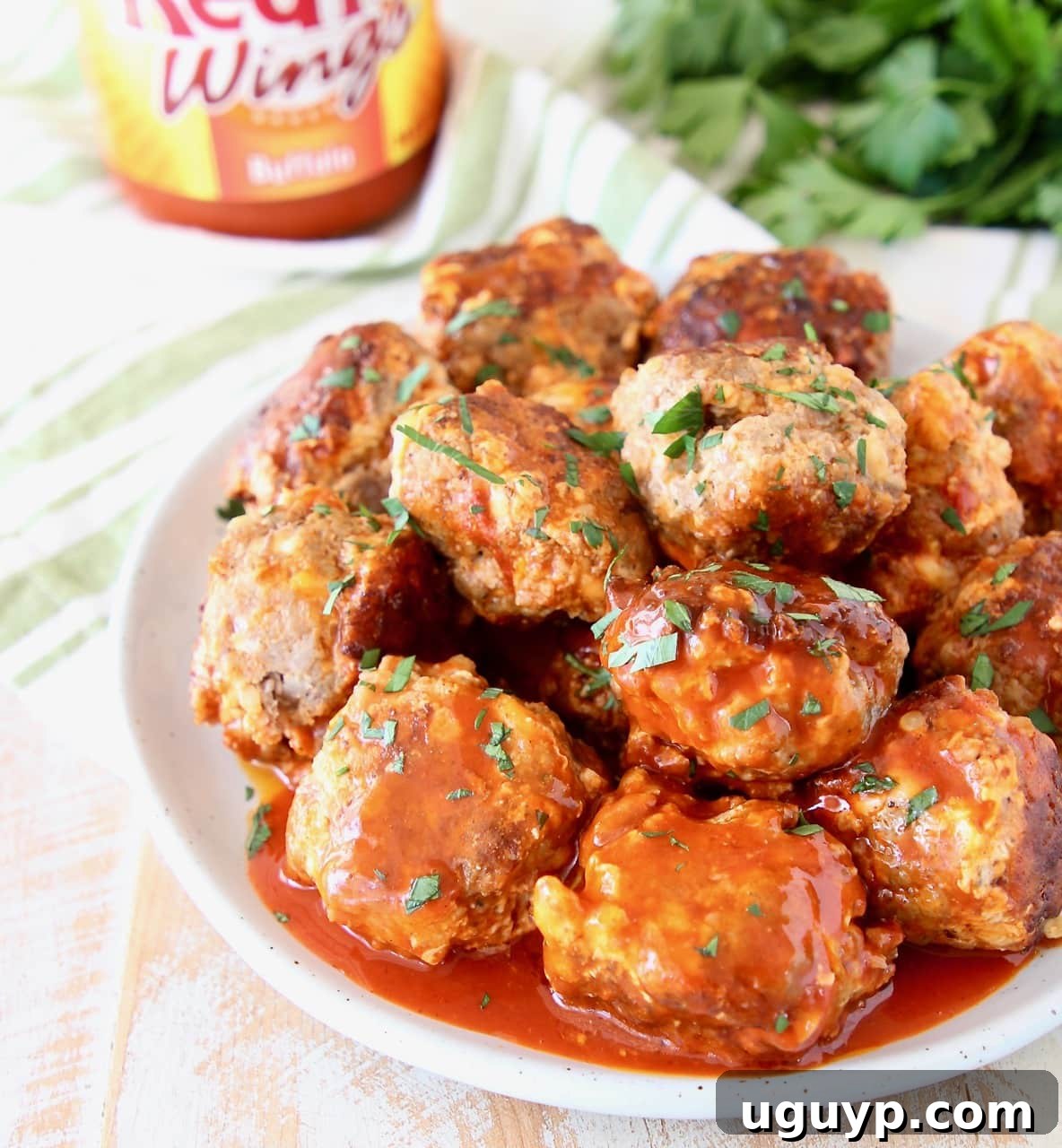 Sausage Balls with Buffalo Sauce on a plate with a jar of Franks Buffalo Sauce and Fresh Cilantro