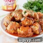 Sausage Balls with Cream Cheese covered in buffalo sauce on plate with jar of buffalo sauce and fresh cilantro