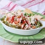 Italian 5 layer dip topped with tomato basil bruschetta in a white serving bowl sitting on a green plate with pita chips