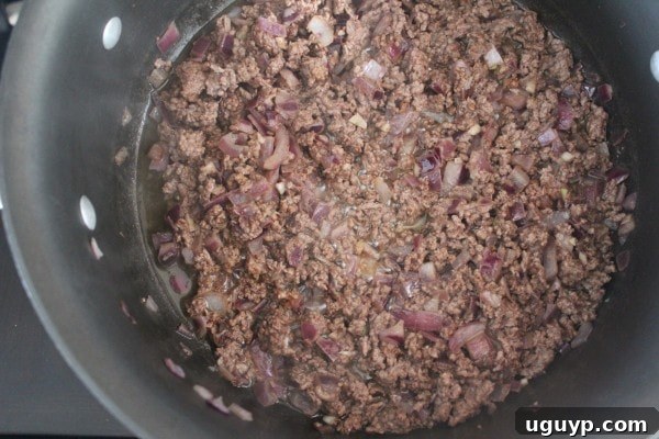 Sautéing diced onions and ground beef in a large pot on the stove, the foundation of our Mediterranean-spiced dish.
