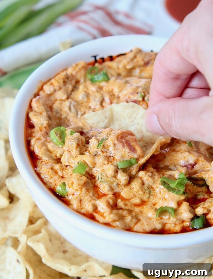 Hand dipping a tortilla chip into a bowl of creamy Buffalo Cheeseburger Dip