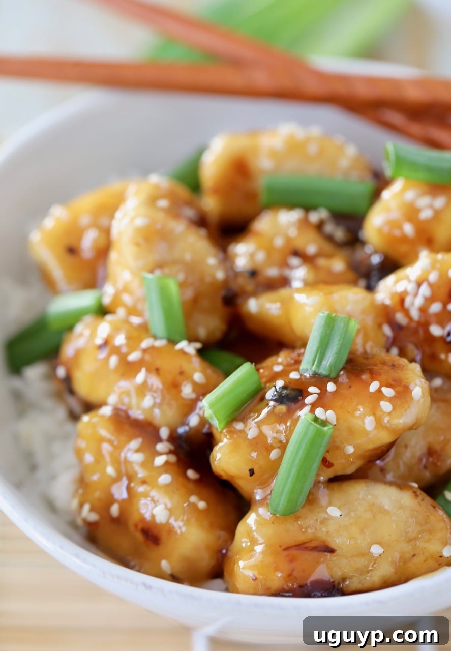 Close-up shot of individual pieces of Chinese honey chicken in a white bowl, generously topped with vibrant green onions and crunchy sesame seeds.