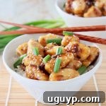 Close-up of golden Chinese honey chicken in a white bowl, with brown chopsticks resting on the side and a scattering of fresh green onions and sesame seeds.