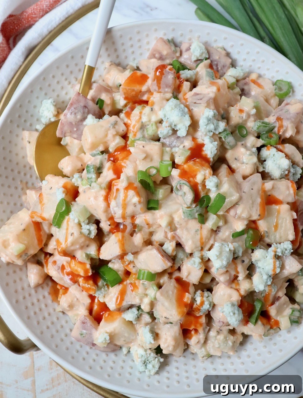 Creamy Buffalo Potato Salad in a large bowl, garnished with a drizzle of buffalo sauce and fresh green onions, with a serving spoon nestled within.