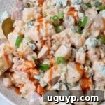 Buffalo Potato Salad in bowl topped with a drizzle of buffalo sauce and a spoon