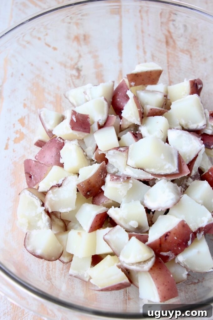 Perfectly boiled and cubed red potatoes ready for mixing in a large clear glass bowl, showcasing their vibrant color and tender texture.