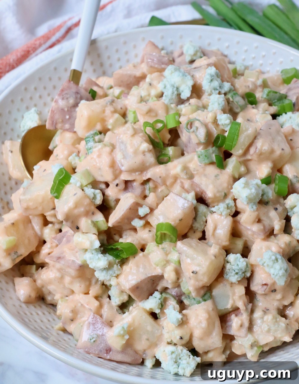 Generous serving of Buffalo Potato Salad in a white bowl with a spoon, ready to be enjoyed, alongside a small dish of extra buffalo sauce.