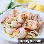 Shrimp on top of pasta on plate with gold fork swirling pasta on the side of the plate