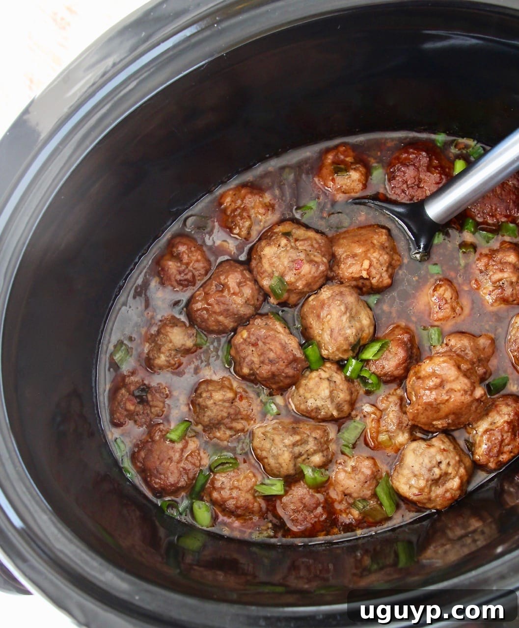 Korean meatballs in a slow cooker, generously coated in rich Korean BBQ sauce, with a serving spoon tucked inside.